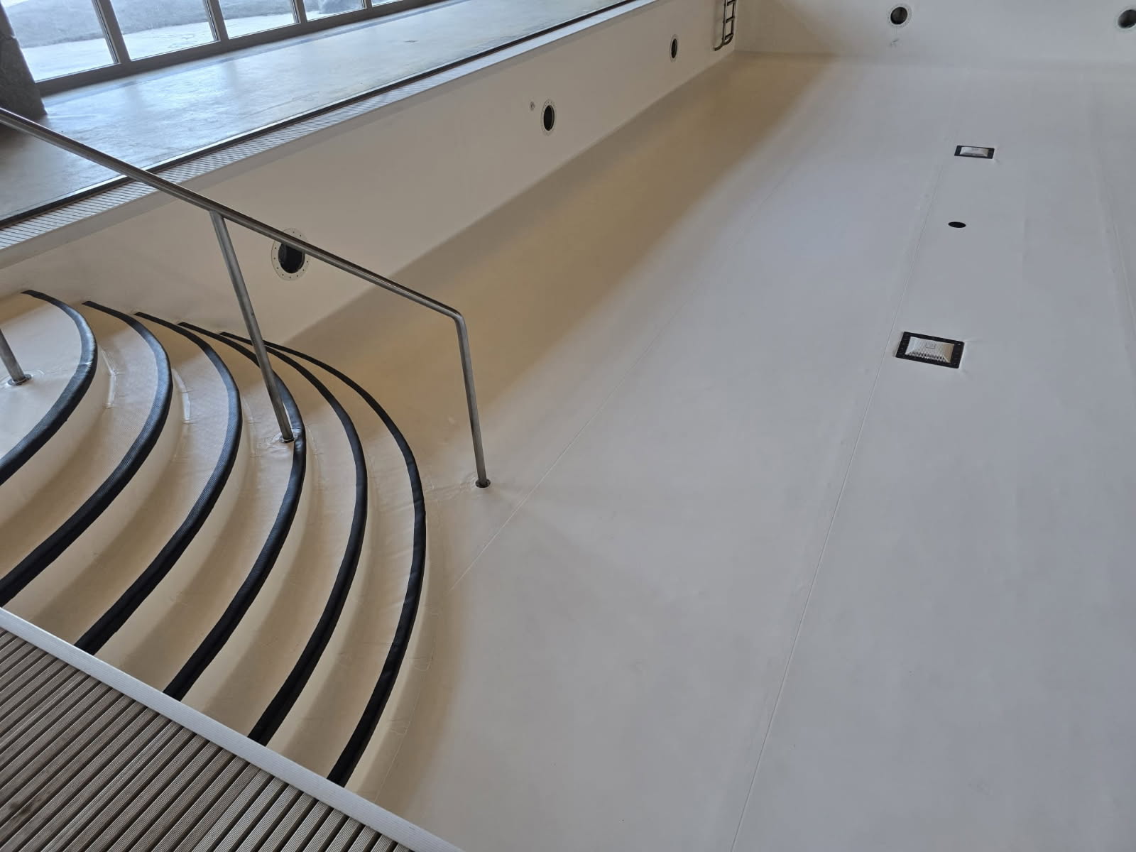 Empty indoor swimming pool with curved steps and handrail